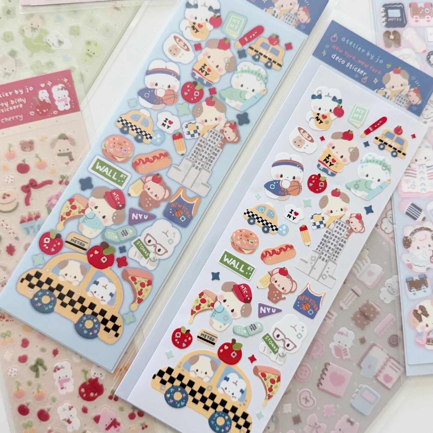 Two sheets of cute cartoon animal stickers displayed on a light surface, featuring characters in checkered cars, hats, and food motifs, with additional sticker sheets partially visible around them.