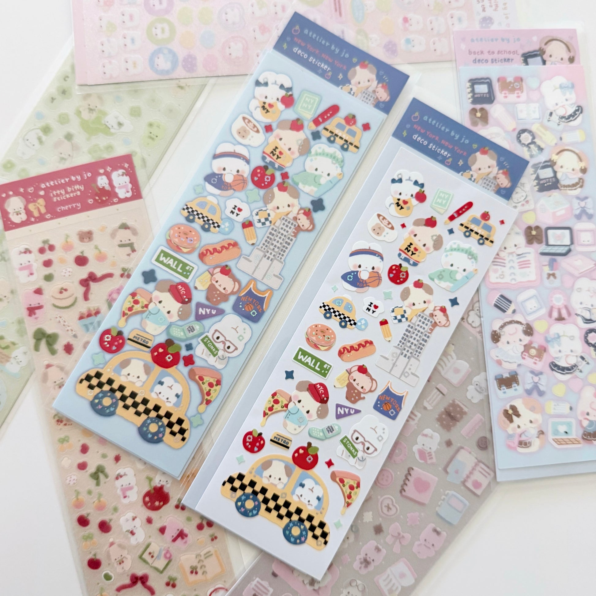 Several sheets of cute cartoon stickers arranged on a white surface. The main visible sheets feature pastel characters, food items, and small icons in blue, pink, beige, and red tones.
