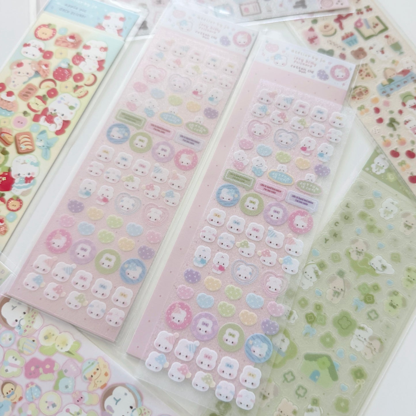 Several sheets of cute pastel stickers laid out on a white surface, featuring cartoon faces, bows, and small decorative motifs in pink, blue, yellow, green, and lavender.