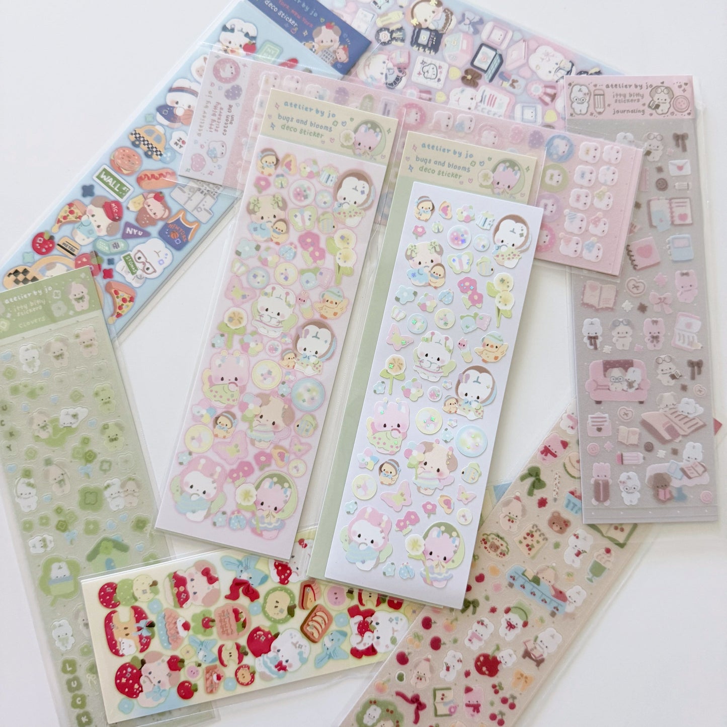Two sheets of pastel colored character stickers with bubble and floral detailing on a white background with various multicolored sticker sheets laying around