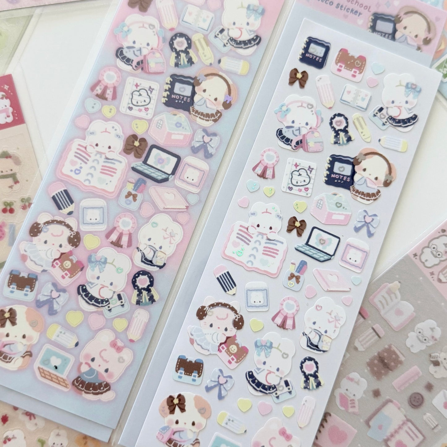 Two sheets of cute pastel school-themed stickers displayed on a light surface, featuring cartoon characters, books, laptops, bows, and small accessories in soft pink, blue, and cream tones.