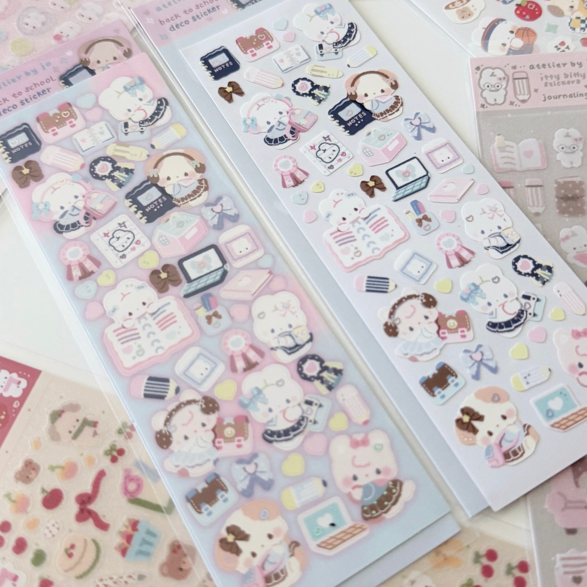 Three sheets of cute pastel stickers featuring cartoon characters, school supplies, and small accessories, arranged on a light surface.