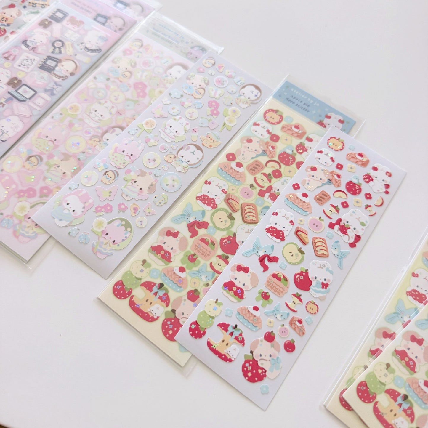 Several sheets of cute cartoon stickers arranged on a white tabletop. The stickers feature pastel characters and food illustrations including strawberries, cakes, and small animal faces.