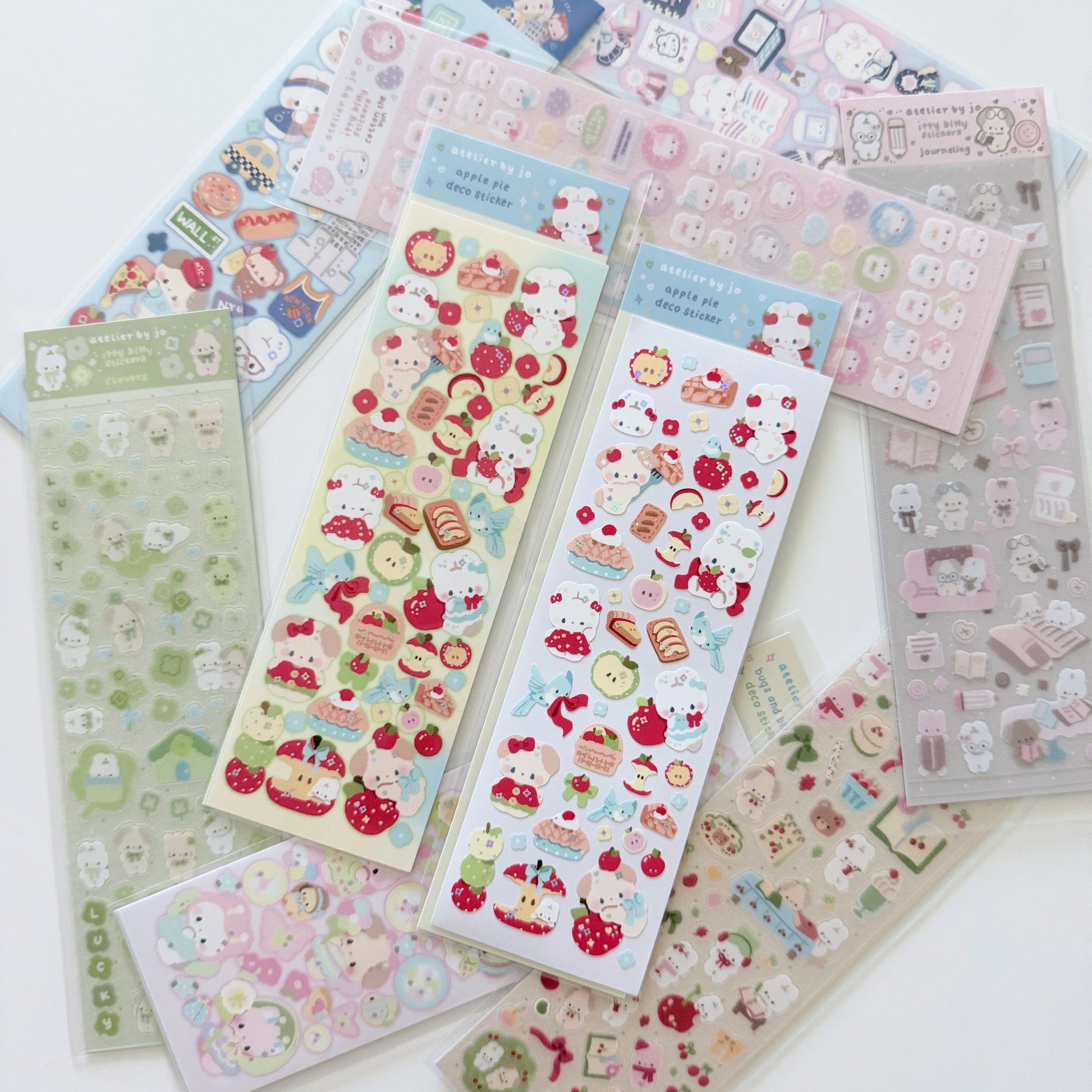 Two sheets of cute character stickers with red and green apple details set on a white background with various other sticker sheets