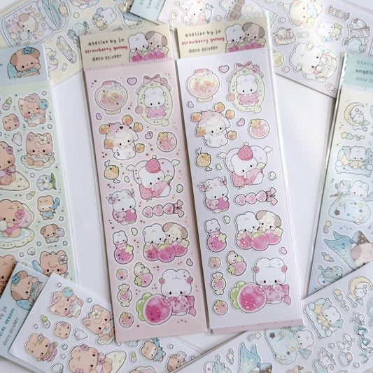 Two sheets of cute strawberry-themed sticker stickers displayed on a white surface, surrounded by other pastel sticker sheets. The main product features a white bear character wearing a pink dress and holding a strawberry, with other cute illustrations like strawberries, hearts, and flowers.