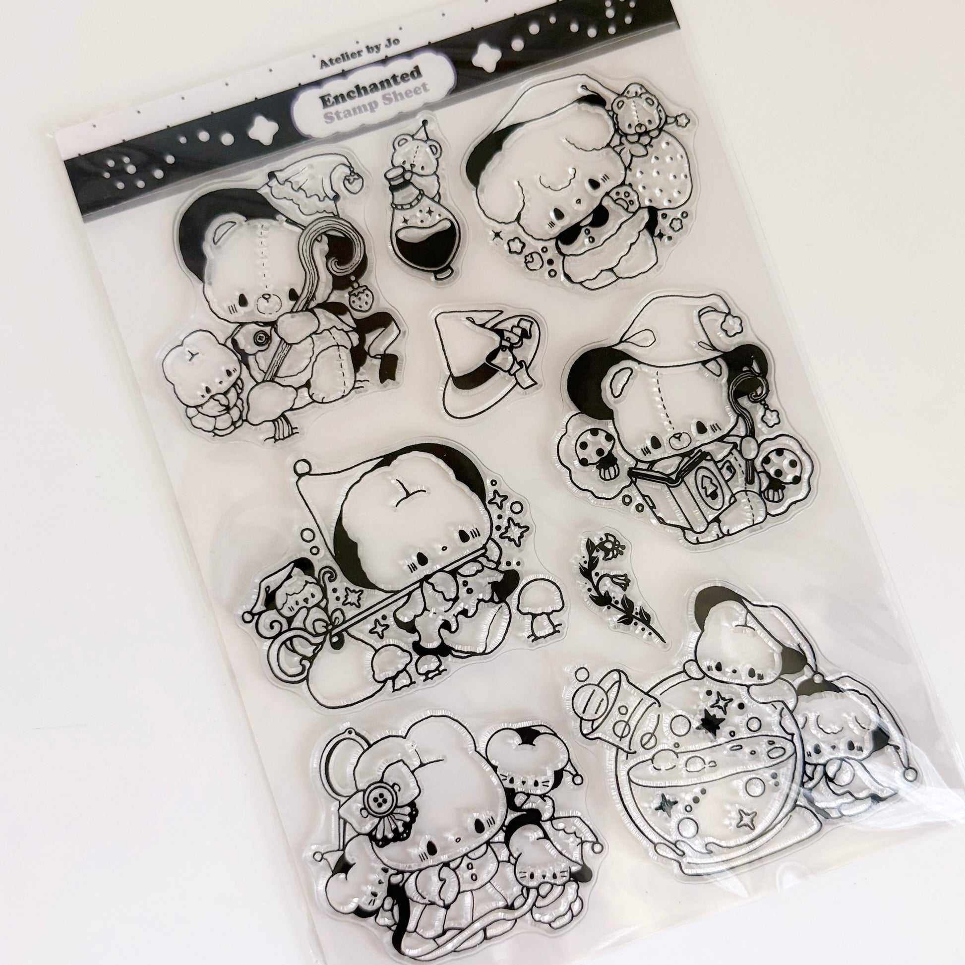 A clear plastic bag containing black-and-white cartoon character stamp designs, photographed on a plain white background. The packaging header reads 'Enchanted Stamp Sheets' 