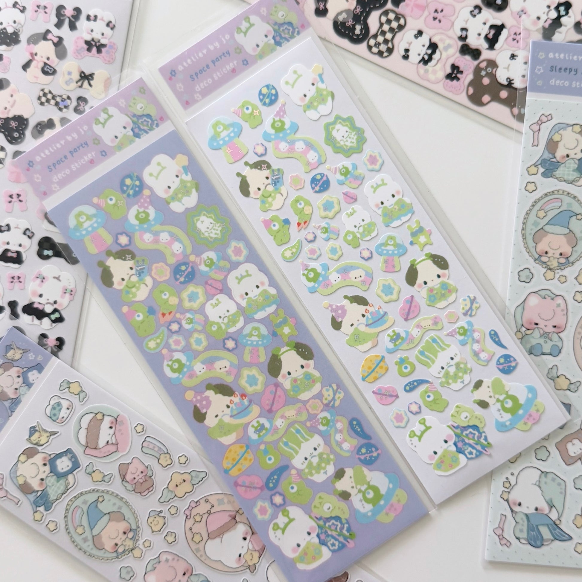 Several sheets of cute cartoon stickers arranged on a white surface. The stickers feature pastel-colored animal characters, flowers, stars, and decorative motifs in soft shades of green, lavender, pink, blue, and black-and-white.