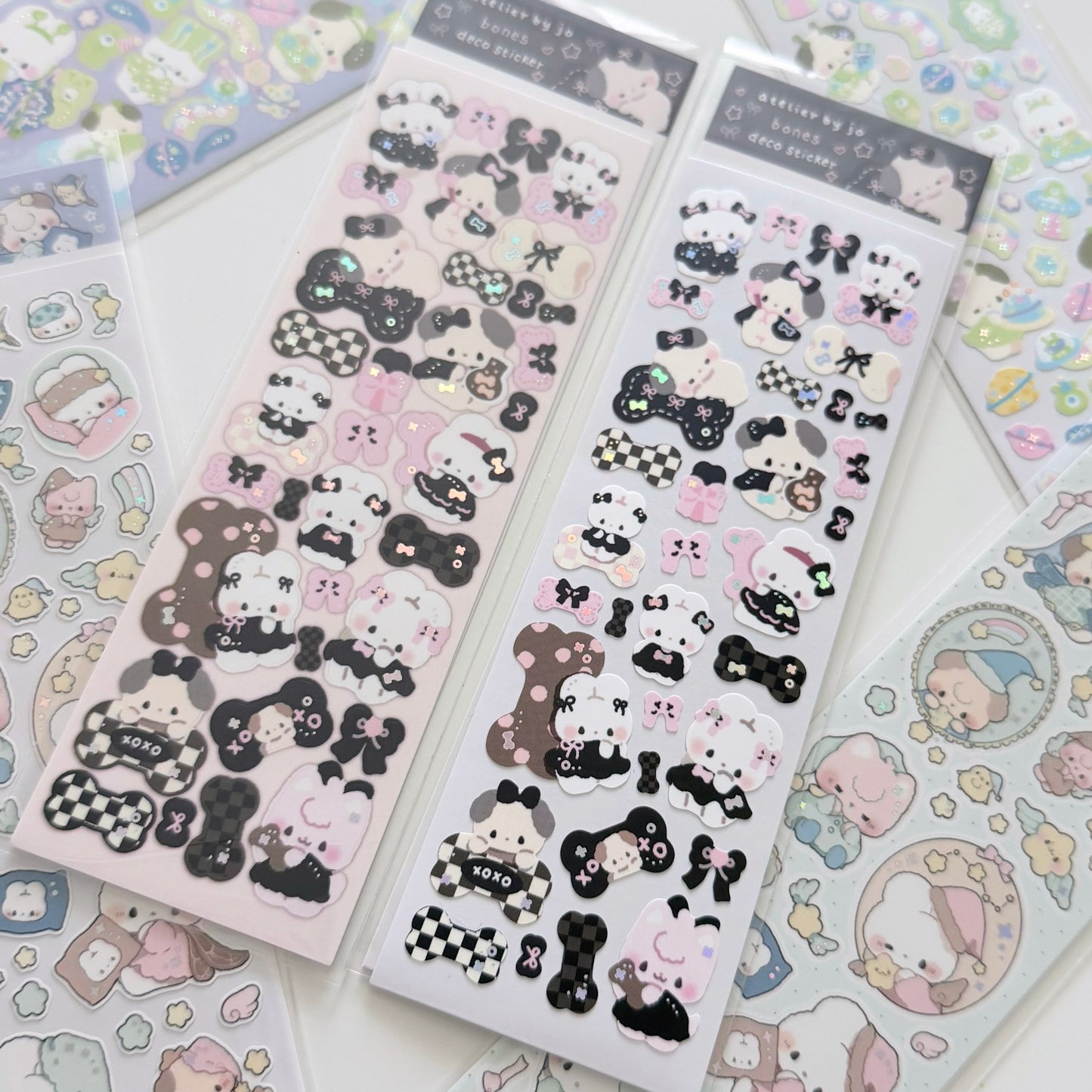 Two packages of cute cartoon character stickers, featuring black-and-white and pink-and-white designs, displayed on a white surface with other sticker sheets partially visible.