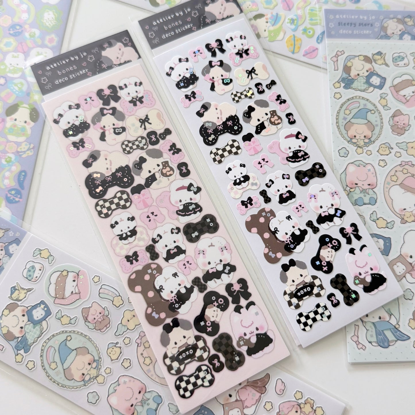 Several sheets of cute cartoon stickers arranged on a white surface. The main visible sheets feature black-and-white character designs with bows, checkered patterns, and small text, while other pastel sticker sheets are partially visible around them.