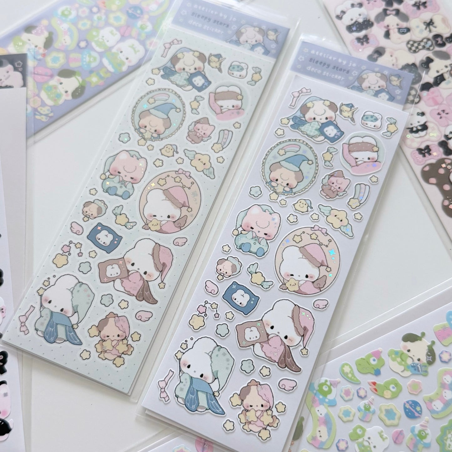 Two packages of cute cartoon sticker sheets featuring pastel-colored characters, displayed on a white surface with other sticker sheets partially visible around them.