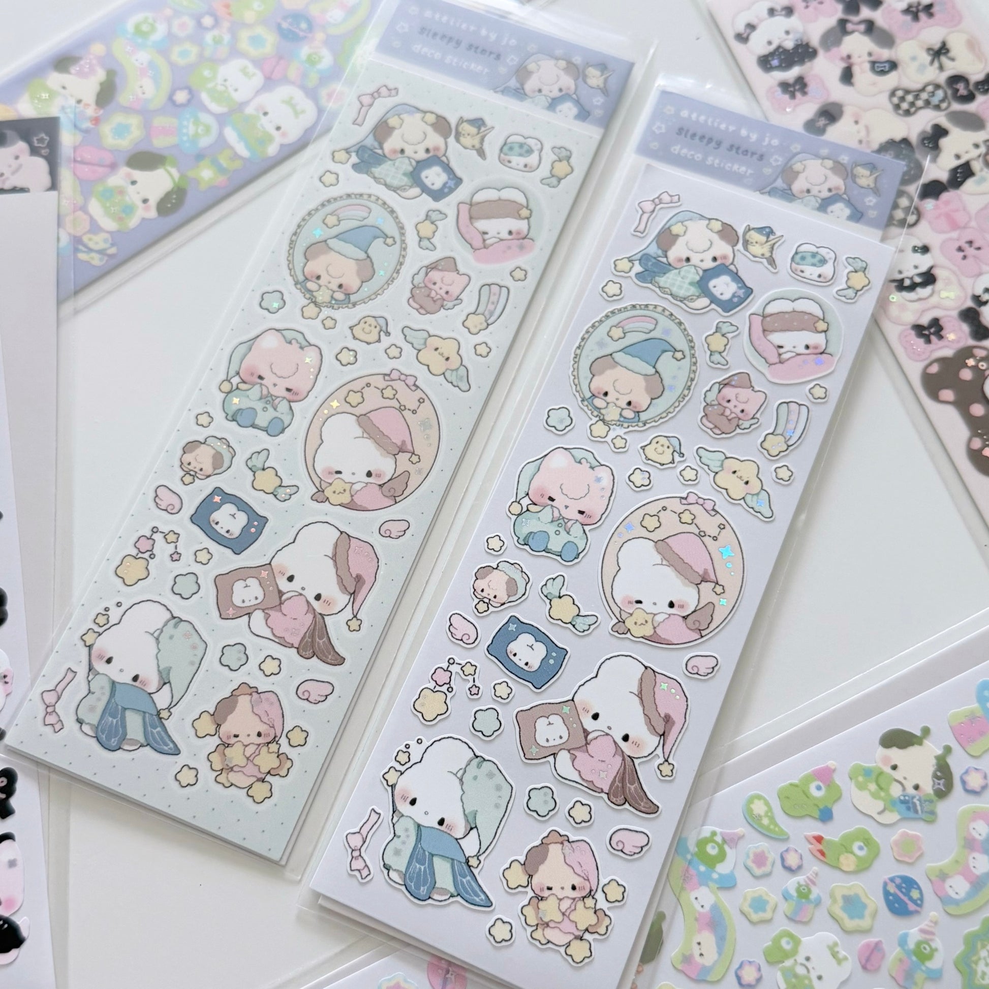 Two packages of cute cartoon sticker sheets featuring pastel-colored characters, displayed on a white surface with other sticker sheets partially visible around them.