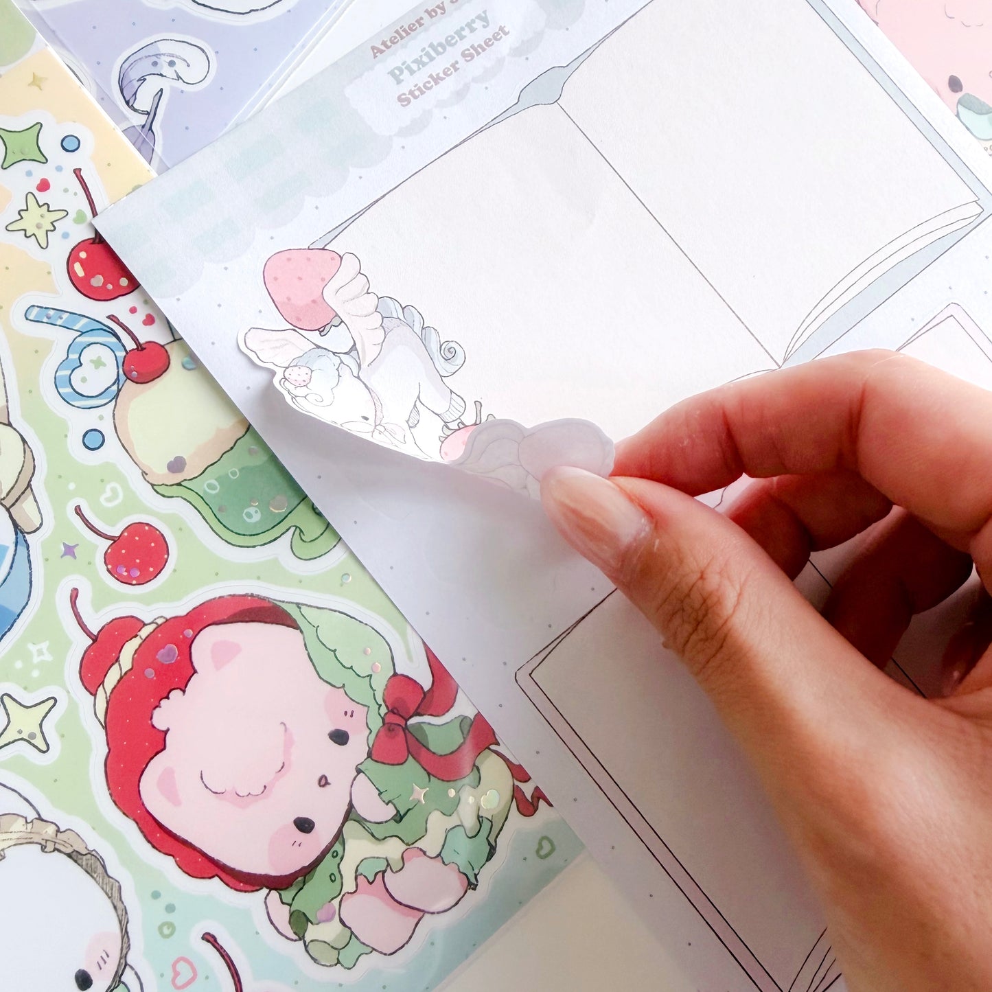 Hand holding a sticker sheet with cartoon characters, surrounded by more stickers on a white background.