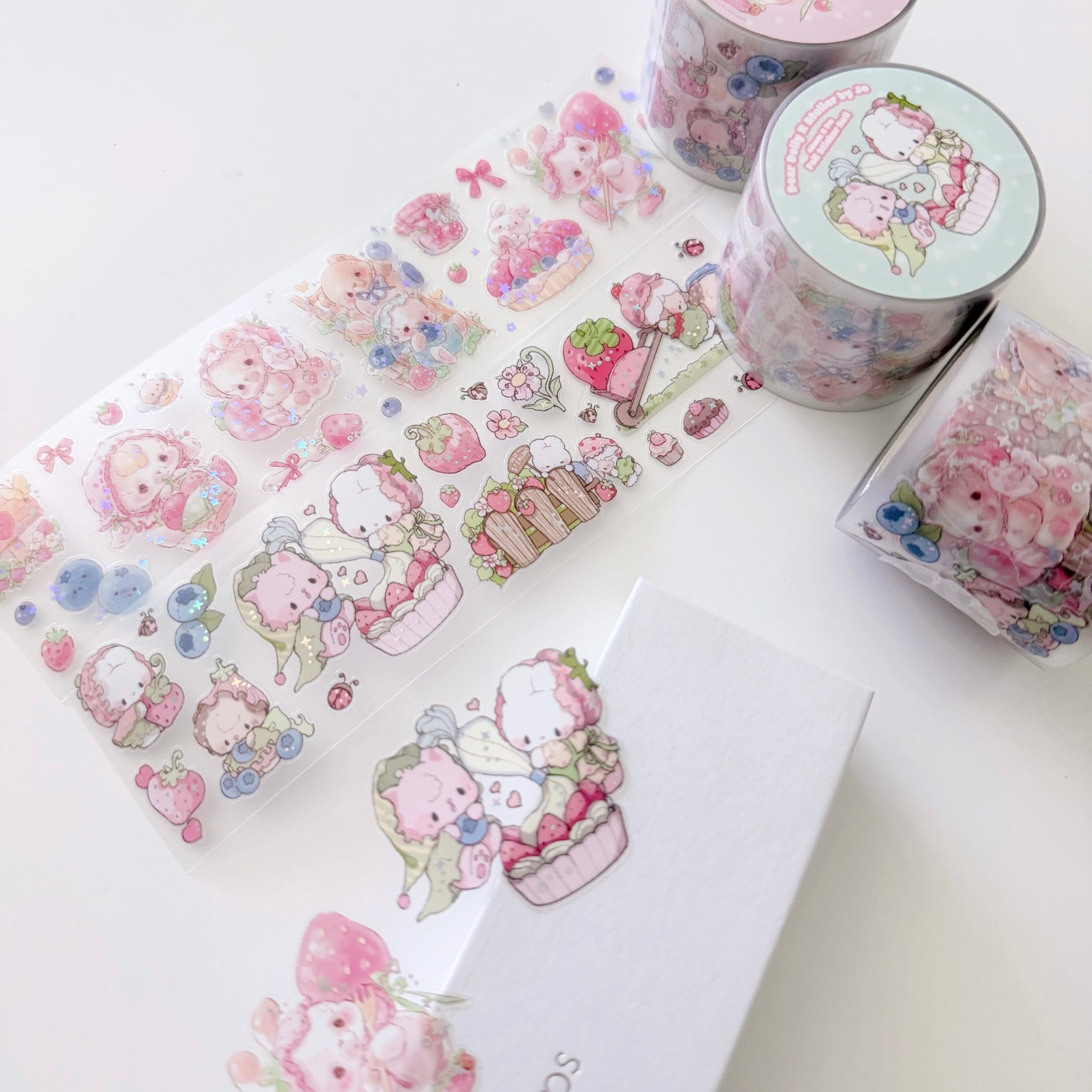 A set of cute pastel washi tape rolls and sheets featuring cartoon characters, strawberries, cupcakes, and small decorative motifs, arranged on a white surface with a white box.